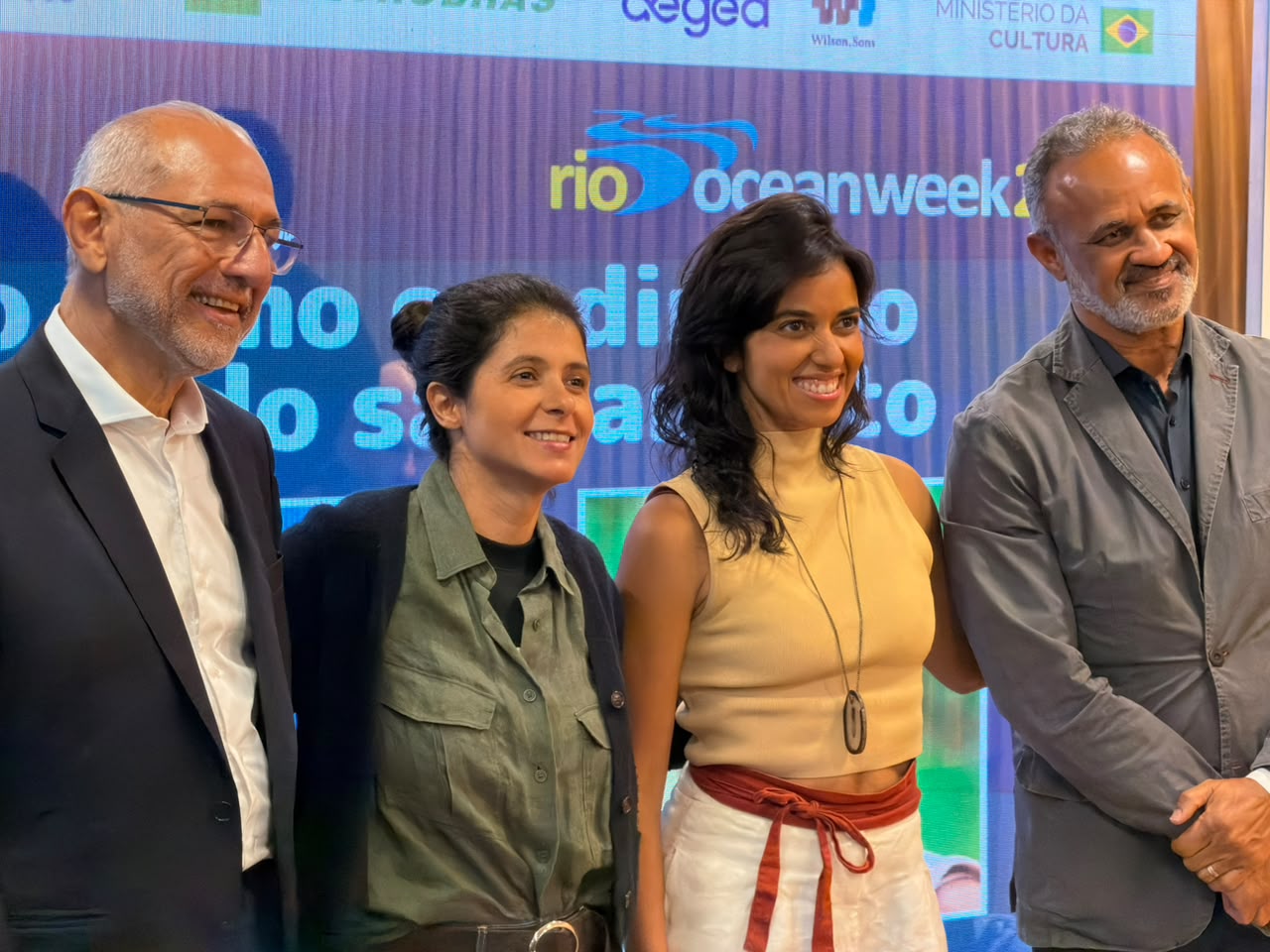 Quatro participantes posam diante do painel da Rio Ocean Week após debate sobre saneamento básico.